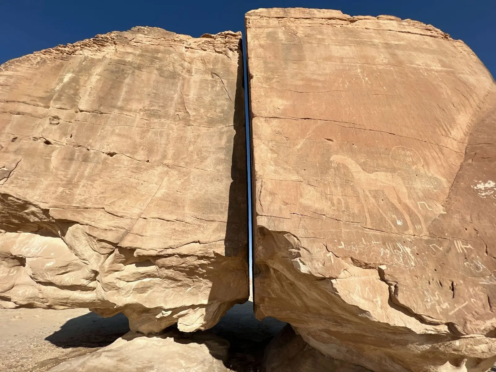 A huge boulder split by a straight vertical crack, standing in open desert.