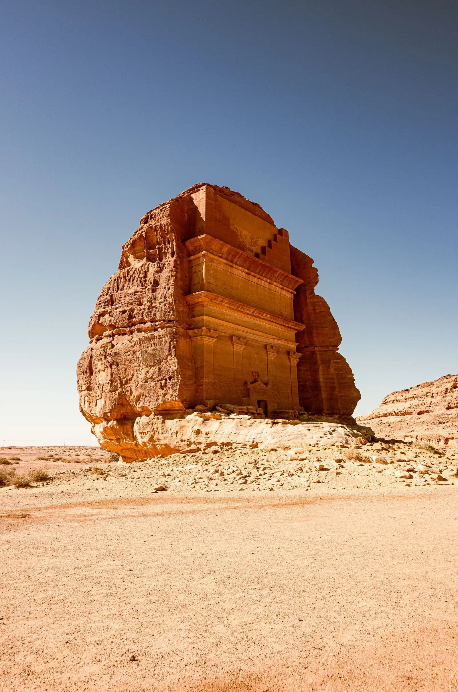 A solitary rock-cut tomb with a carved facade standing in open desert.